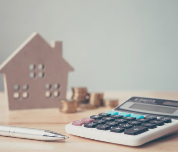 Calculator with wooden house and coins stack and pen on wood table. Property investment and house mortgage financial concept